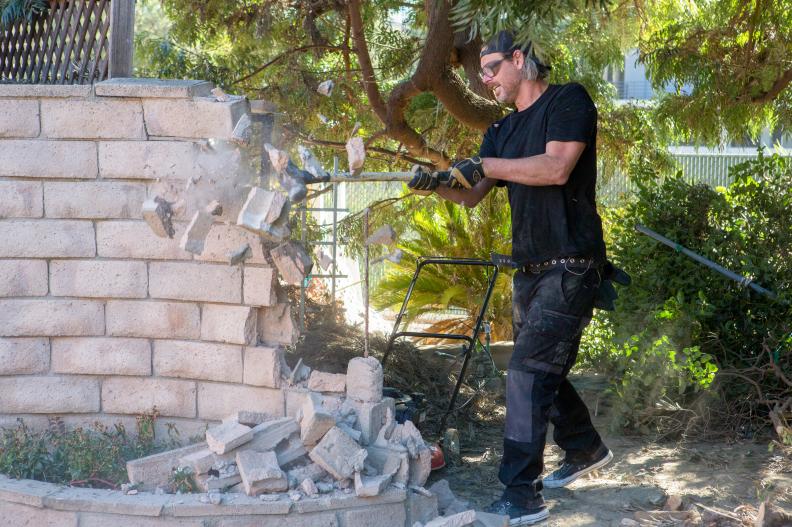 HGTV's Steve Ford uses a sledge hammer to demo an old wall in the backyard of the original Brady House in Studio City, CA, as seen on A Very Brady Renovation.