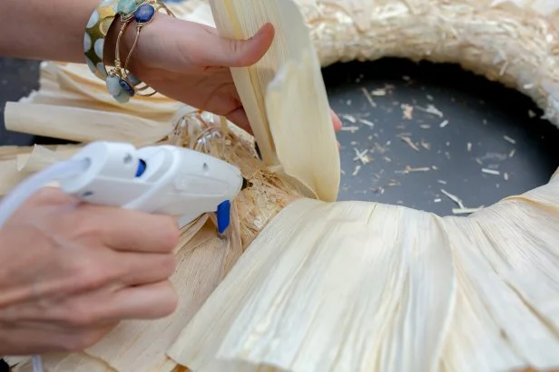 For the final layer, wrap the husks around the wreath form and secure to the back using pins or hot glue. Next, hot glue the bottom of the husks to the front of the form.