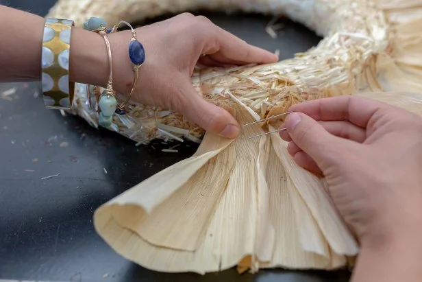 Attach the husk the bottom of the wreath form with a floral pin. Repeat this process around the form, slightly overlapping the husks as you go.