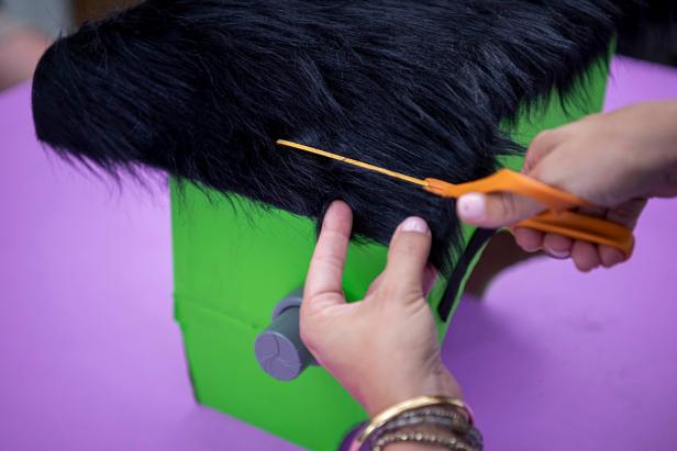 Use hot glue to attach faux fur to the top of the box for the hair and felt strips to the front for eyebrows. Give the faux fur a haircut to make it even on all sides.