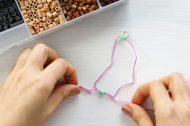 Add a bead by threading the needles through opposite sides of the bead. Continue adding beads by looping the ends of the string back and forth through them.