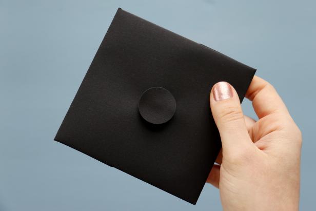 Use a circle punch or scissors to cut out a circle out of the black paper. Next, glue the button onto the center of the cap. Then, glue the paper circle on top of the button.