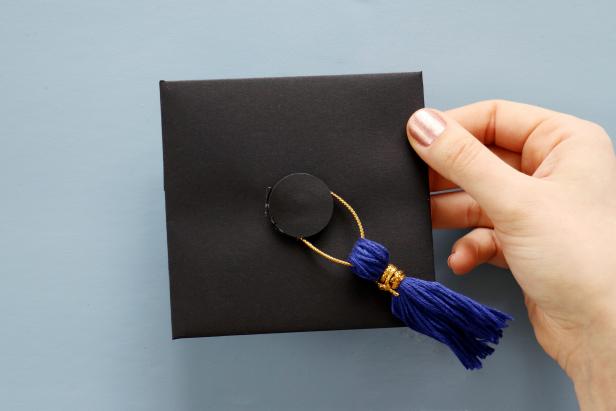 For the tassel, wrap embroidery thread around your fingers 30 times. Wrap the metallic string around the top then cut through the bottom loop with scissors to reveal the tassel. Thread more string through the top of the tassel and glue it around the button to get a mini graduation cap design.