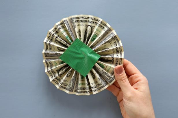 Accordion fold five bills. This step works best with newer, crip bills instead of worn bills. Tape the ends together to get a large loop and carefully press it together into a medallion shape. Use small pieces of duct tape on both sides to lightly hold it together.