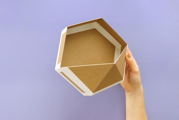 Using masking tape, attach the six rectangles around the hexagon. Fold up each rectangles and tape together. Cover all outside seams with masking tape to ensure a strong hold. Then, attach the triangular piece with more masking tape to finish off the structure of the planter.