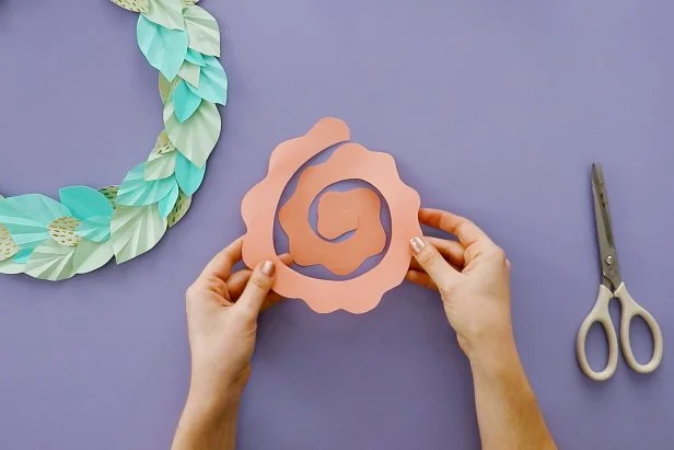 Make a flower by cutting a spiral into another piece of origami paper. Cut a wave into the outside edge of the spiral. Roll it up to get a flower shape. Put down a dollop or hot glue onto a piece of cardstock and press the flower down onto it. Once it dries, cut it out from the cardstock.