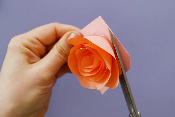 Make a flower by cutting a spiral into another piece of origami paper. Cut a wave into the outside edge of the spiral. Roll it up to get a flower shape. Put down a dollop or hot glue onto a piece of cardstock and press the flower down onto it. Once it dries, cut it out from the cardstock.