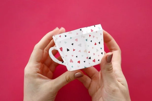 Cut out the handle from the pattern. Apply glue to just the handle and not the tab on the side. Glue it to the same scrapbook paper and cut out to get a two-sided handle. Fold the tabs back and push them through the line you cut earlier. Glue in place to form the teacup handle.