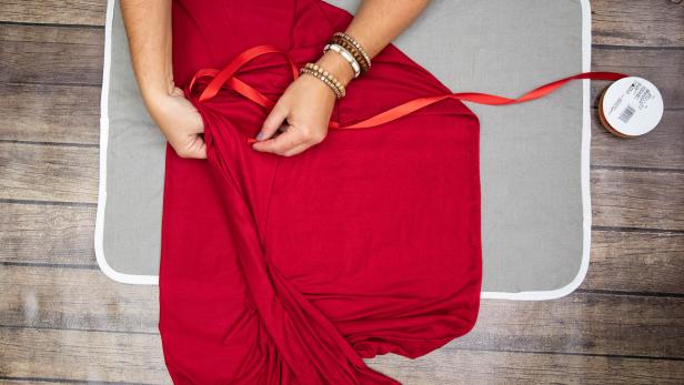 This red ribbon is being threaded through red jersey fabric for a Little Red Riding Hood Halloween costume. The no-sew DIY options is budget-friendly and easy to make.