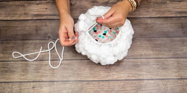 A shower cap is used to make a DIY wig for a Big Bad Wolf dog costume. The shower cap has had cotton balls glued across the entirety of the top and white twine tied through holes to hold on the dogs head.