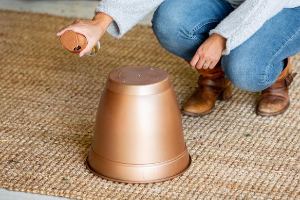 This plastic planter has been painted with metallic spray paint to resemble a metal bell. The planter is being turned into an oversized Christmas bell to decorate a front porch.