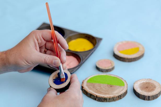 A small paintbrush is used to apply brightly colored acrylic paint to craft wood rounds.