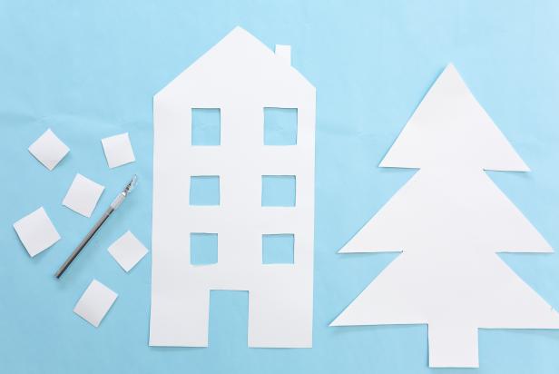 This poster board has been cut out using a craft knife to create the shape of a building and a tree. The pieces will be mounted on a window using double-side tape to create a paper Christmas village.