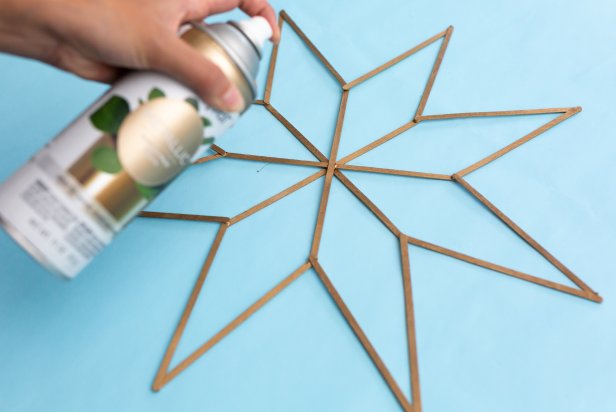 This Scandinavian star decoration is made from wooden coffee stir sticks that have been glued together with hot glue. Gold metallic spray paint is used to give the star a shine.