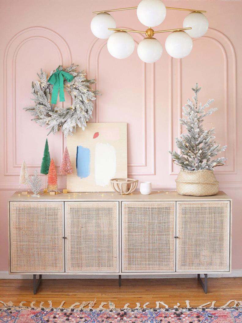Hot Pink Pineapple blogger Cyn dressed up her chic cane sideboard with a frosted mini tree and a sweet wreath. Cute and colorful evergreen trees add bursts of saturated color, while abstract art gives the space a uniquely modern touch.