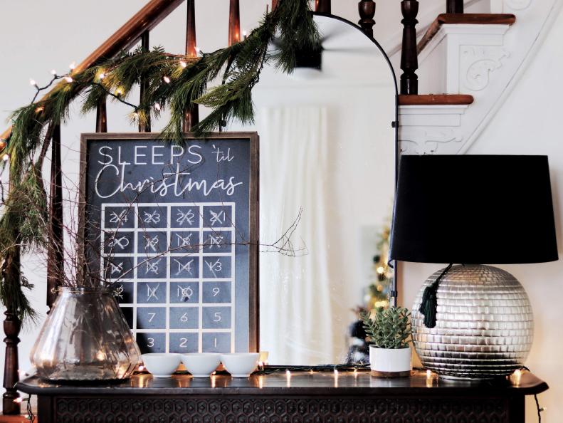 An arched black mirror sets the foundation for blogger Made by Carli's sleek New England entryway. Nixing red for darker shades, she layered a chalkboard advent calendar under classic garland. A black velvet lamp shade and hints of gold glam it all up.