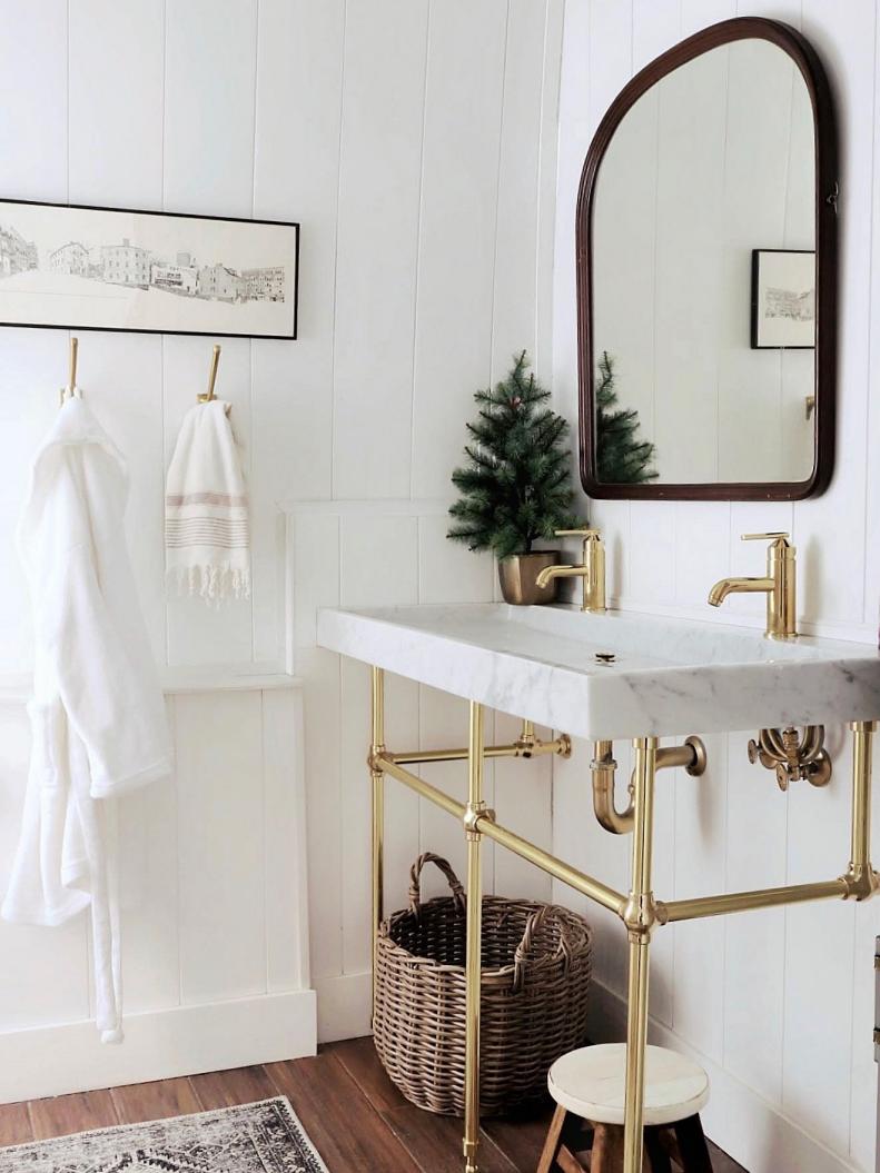 Yes, you can maintain a minimal aesthetic and still get festive. Made by Carli placed a mini evergreen in a golden pot in her bathroom and it's so adorable. Gold hardware on the sink gives her look an extra pop.