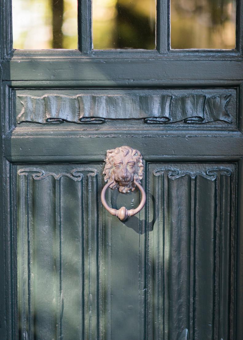 A dark green door features scrollwork and a lion knocker.