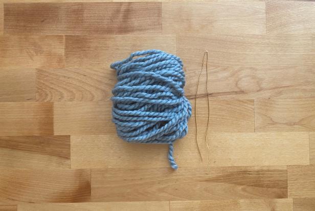 Trim the yarn and carefully remove the bundle from the cardboard. Now place the bundle on the workstation so the loops are facing a horizontal direction. Next, use a 14’’ piece of jewelry wire and fold it in half.