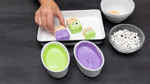 These crispy rice treats have been cut in pieces and dipped in purple and green white chocolate to create crispy rice monster treats for Halloween. Candy eyeballs finish off the monster look.