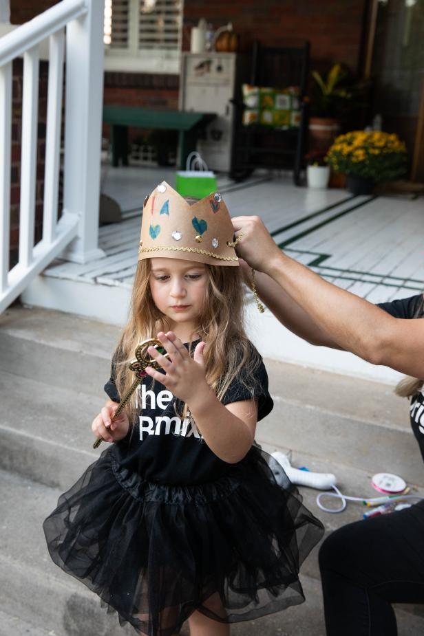 This queen Halloween costume is being made complete with the addition of a paper bag crown. The crown was cut out of a paper grocery bag using scissors and decorated with stick-on jewels and markers to look beautiful on this little queen while she trick-or-treats.