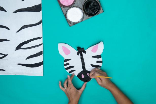 This paper bag zebra mask has been cut out of a large paper grocery bag and painted to resemble a zebra. Black and white paint make up the zebra skin while pink accents have been added to make the design pop.