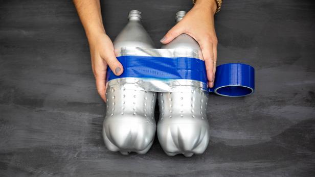 Tape is wrapped around two 2-liter bottles that have been painted silver to look like a jetpack. The tape both holds the bottles to each other as well as serves a decorative purpose.