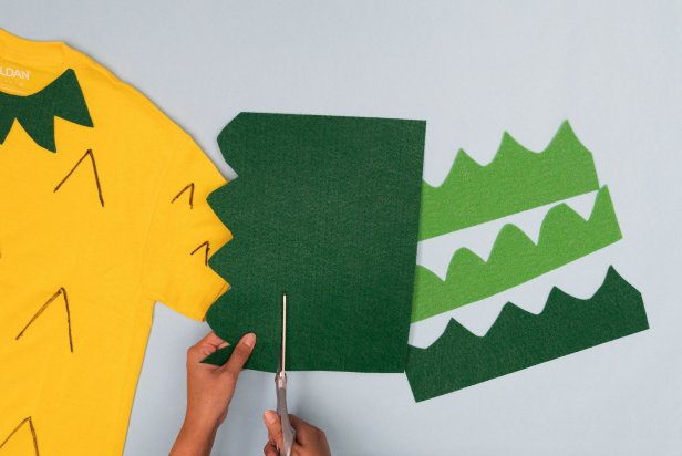 This green felt is being cut out using scissors to be rolled into a pineapple top for a pineapple Halloween costume made from a t-shirt.