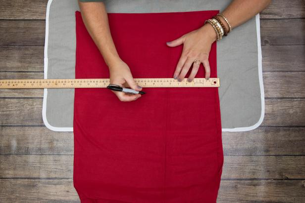 Dots are being drawn at specific measurements against a yard stick sitting on red jersey fabric. The fabric is being used to make a Little Red Riding Hood costume for Halloween.