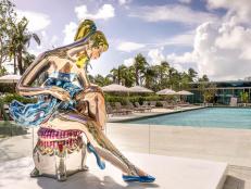 A high-gloss ballerina sculpture stands in front of a pool. 