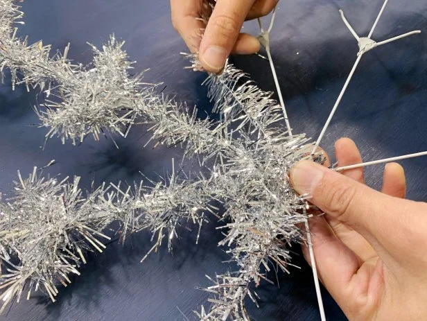 Tightly wrap the entire snowflake with silver tinsel starting at one end of a spoke and continuing until completely covered. Cut the tinsel down to smaller pieces to make it easier to wrap. TIP: If the tinsel does not have wire, use a hot glue gun to glue down the edges