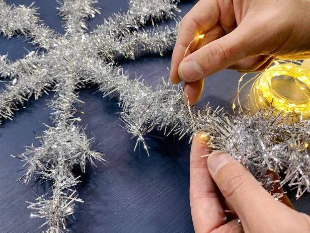 Place the battery pack in the center of the snowflake and begin to wrap the lights around each spoke. Wrap from the center to the end of each spoke, then back down to the center to then continue on to the next spoke. TIP: Pay close attention to the amount of lights you have as you wrap making sure you have enough to evenly wrap each spoke.