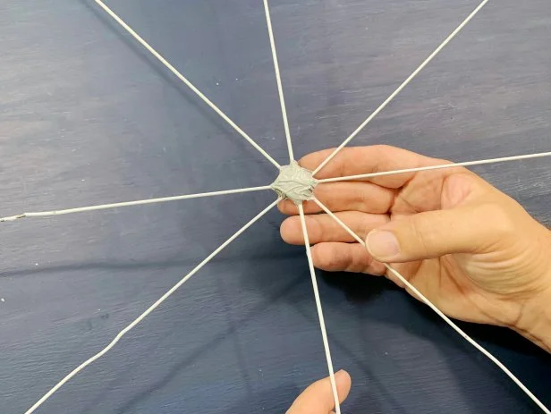 Lay out two hangers to create a plus sign with the center points meeting in the middle. Tape them in place using small pieces of duct tape. Lay the remaining two other hangers in an X shape on top to create your spokes and tape all pieces together to secure. Tip: Use a soldering iron instead of duct tape to make these weather resistant.