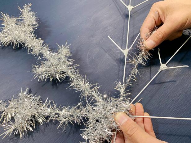 Tightly wrap the entire snowflake with silver tinsel starting at one end of a spoke and continuing until completely covered. Cut the tinsel down to smaller pieces to make it easier to wrap. TIP: If the tinsel does not have wire, use a hot glue gun to glue down the edges