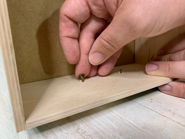 Lay the handle in place and insert the post of the rivet through the hole. The rivet should be large enough to pass through the wood. Carefully turn the drawer and position the cap on the rivet post. Position the rivet onto the anvil then tap with a hammer until secure. Repeat for all handles until each is attached