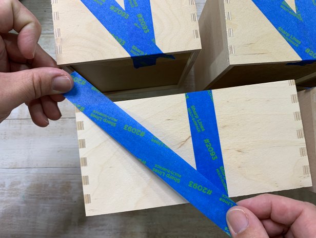 Remove all the drawers and turn them over to the blank backside. Measure and lightly mark the vertical center point. If the drawers are long, split it into thirds or fourths. Use a piece of painters tape longer than the drawer and lay it down diagonally from the top left corner to the bottom marked point to create a right angle triangle. Repeat this process for each drawer. Tip: Before painting, sand down the drawers until they are smooth if needed.