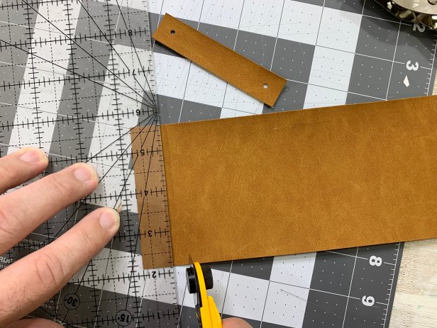 Use a ruler and cutting mat to measure out 8 equal size pieces of faux leather. Cut each handle out using a rotary blade or pair of scissors. Fold each piece in half so that the ends meet. Using punch pilers, punch through both pieces about a  ½ inch from the edge.