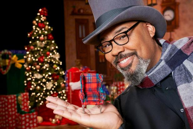 Host James Monroe Iglehart holds a tiny armchair from one of the contestant's challenge homes, as seen on The Biggest Little Christmas Showdown. (portrait)