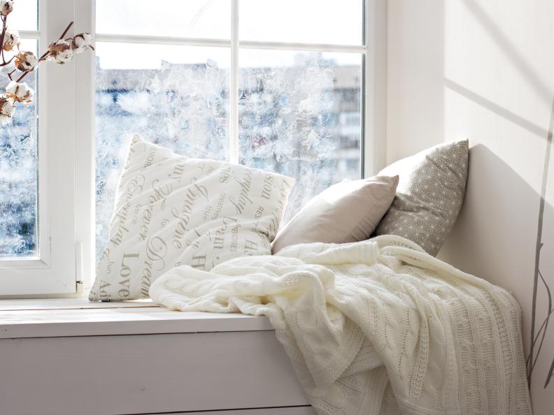 A bright window seat decorated with white throw pillows and blanket
