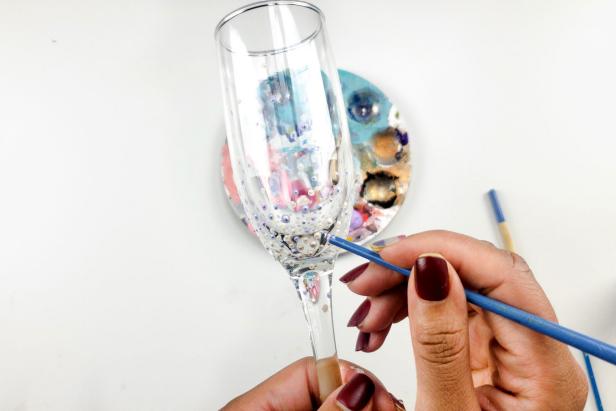 First, make sure the glass champagne flute is clean and dry. Then, add a drop of glass paint to a disposable plate or palette. Next, dip the end of the paintbrush handle into the glass paint. Now gently press the handle onto the glass to create a unique pattern; avoid the rim of the glass completely.