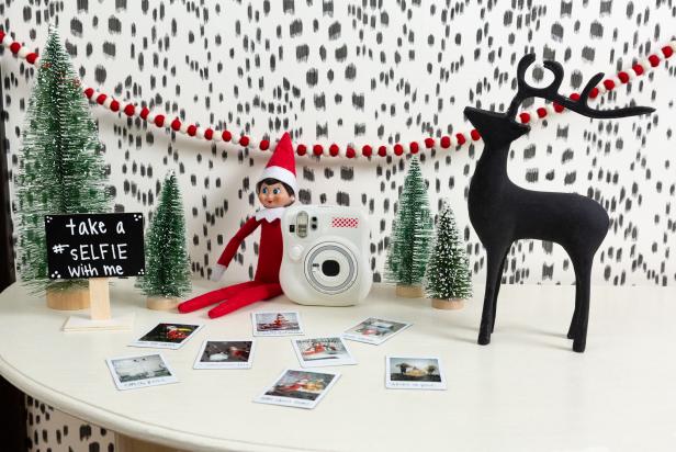 An elf sits on a table with an instant camera and holiday-themed props