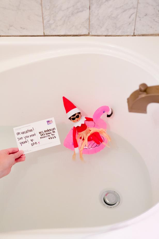 A toy elf on a small float in a bathtub with a goodbye postcard. 