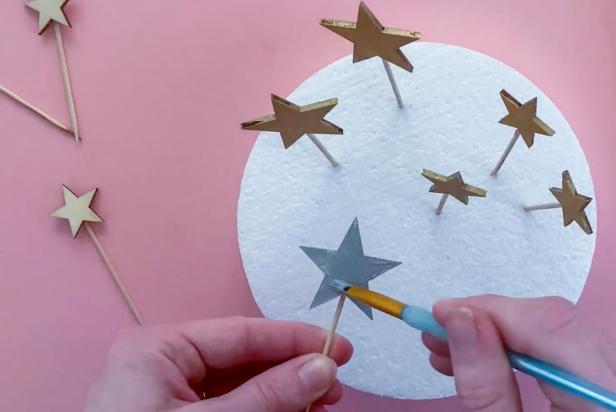 Use a small paintbrush to paint metallic paint onto the wooden stars. Then place them into a mold to dry.