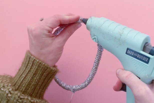 Start by measuring jewelry wire around the plastic headband. Next, cut the cord and wrap the ends of the wire tightly around the middle part of the plastic headband. Then use a low-temp hot glue gun to add a bead of glue to the bottoms of the plastic headband. Now wrap the glitter string starting at the ends and wrapping tightly up the headband. Once to the other end, add a bead of glue from a low-temp hot glue gun to secure ends.