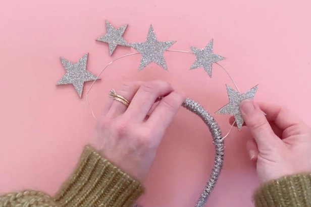 Arrange the wooden stars in a pattern that fits the plastic headband. Next, paint a coat of decoupage glue to the star. Shake a generous amount of glitter onto the star, then let dry. Once dry, add a dot of glue from a low-temp hot glue gun to the back of each wooden star and affix it to the jewelry wire on the headband. Once secure and all the stars are placed on the headband, add another coat of decoupage glue to the back and shake on a generous amount of glitter. Leave the headband to dry for several hours.