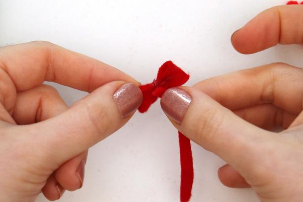 Make a small felt bow by cutting a bulbous shape, a long thin rectangle, and two small ribbon shapes out of red felt. Use hot glue to glue the two ends of the bulbous shape to the center. Then glue the long piece around the center. Finally, glue the two ribbon shapes to the back, to get a small felt bow.