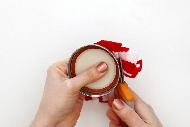 Carefully hold a mason jar lid on top and cut around it to get a circle. Cut out an ornament hanger, two leaves, and a small red circle and glue them in place on the top of the ornament. Add a ribbon to the back to hang.