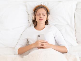 Young woman lying in bed with eyes closed using headphones