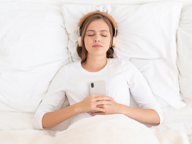 Young woman lying in bed with eyes closed using headphones