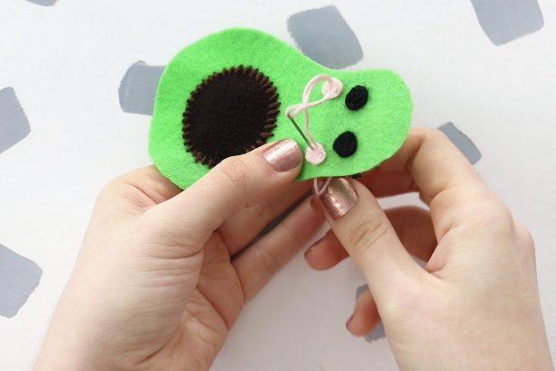 Sew the eyes on the avocado with black thread and the cheeks with pink thread. Add reflections in the eyes with a small piece of white thread as well as a smile from black thread.